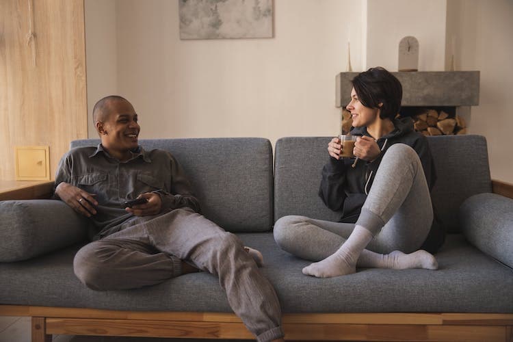Couple sitting together on a sofa at home, talking and smiling, representing connection and communication in couples therapy.